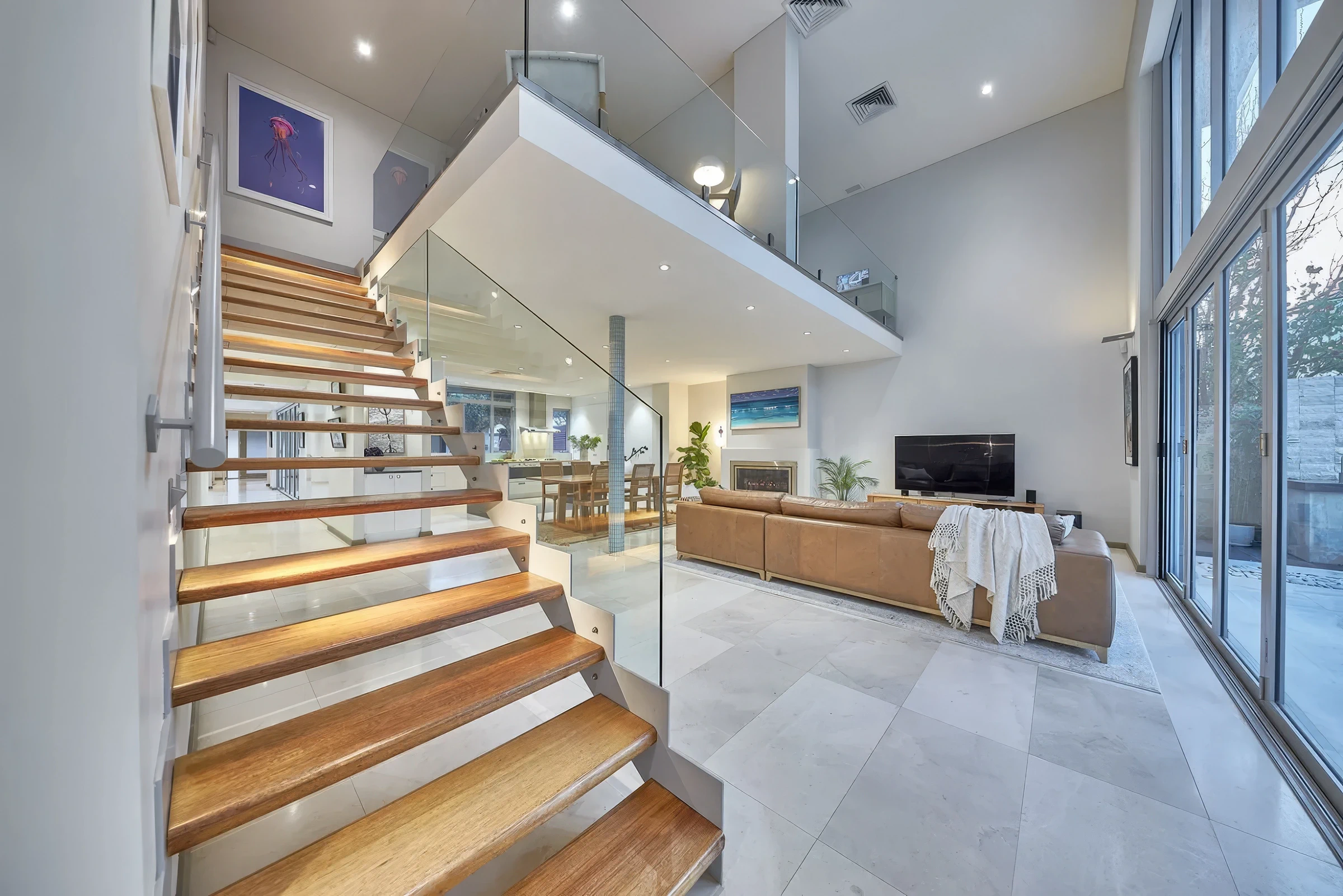 Open-plan living area with wooden staircase and glass balustrades in a modern Australian home