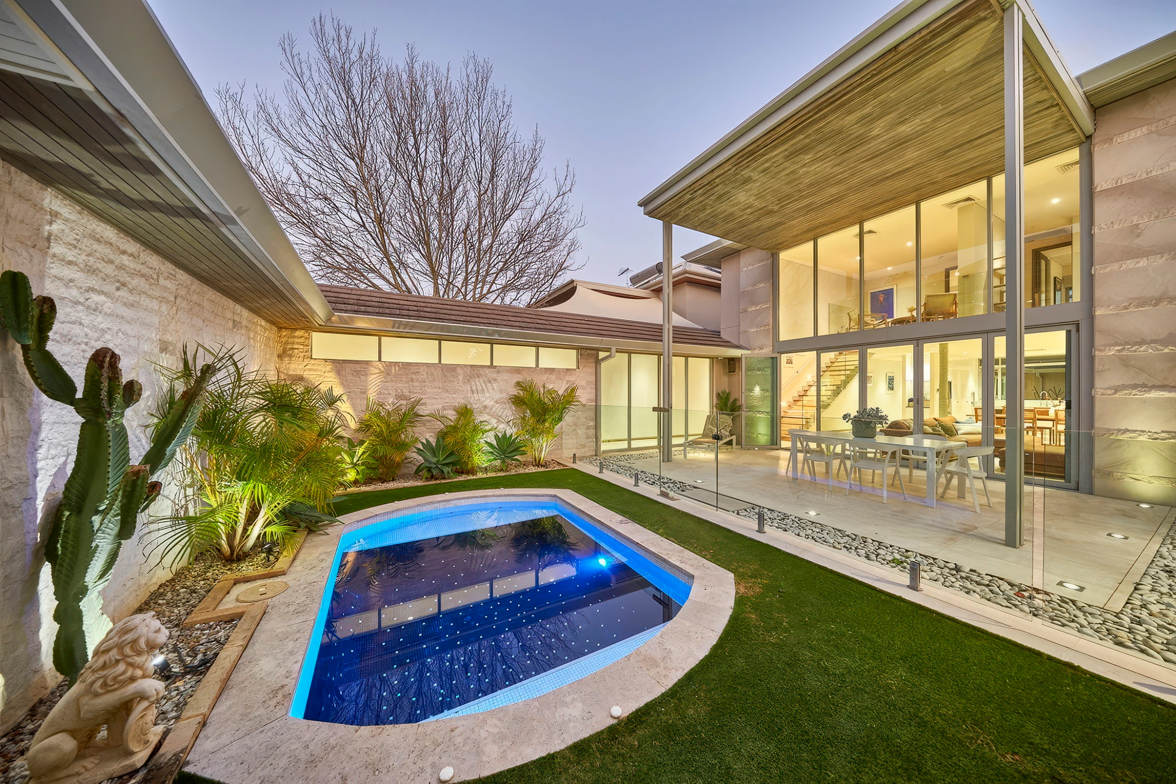 Modern residential backyard with illuminated swimming pool and indoor-outdoor living area