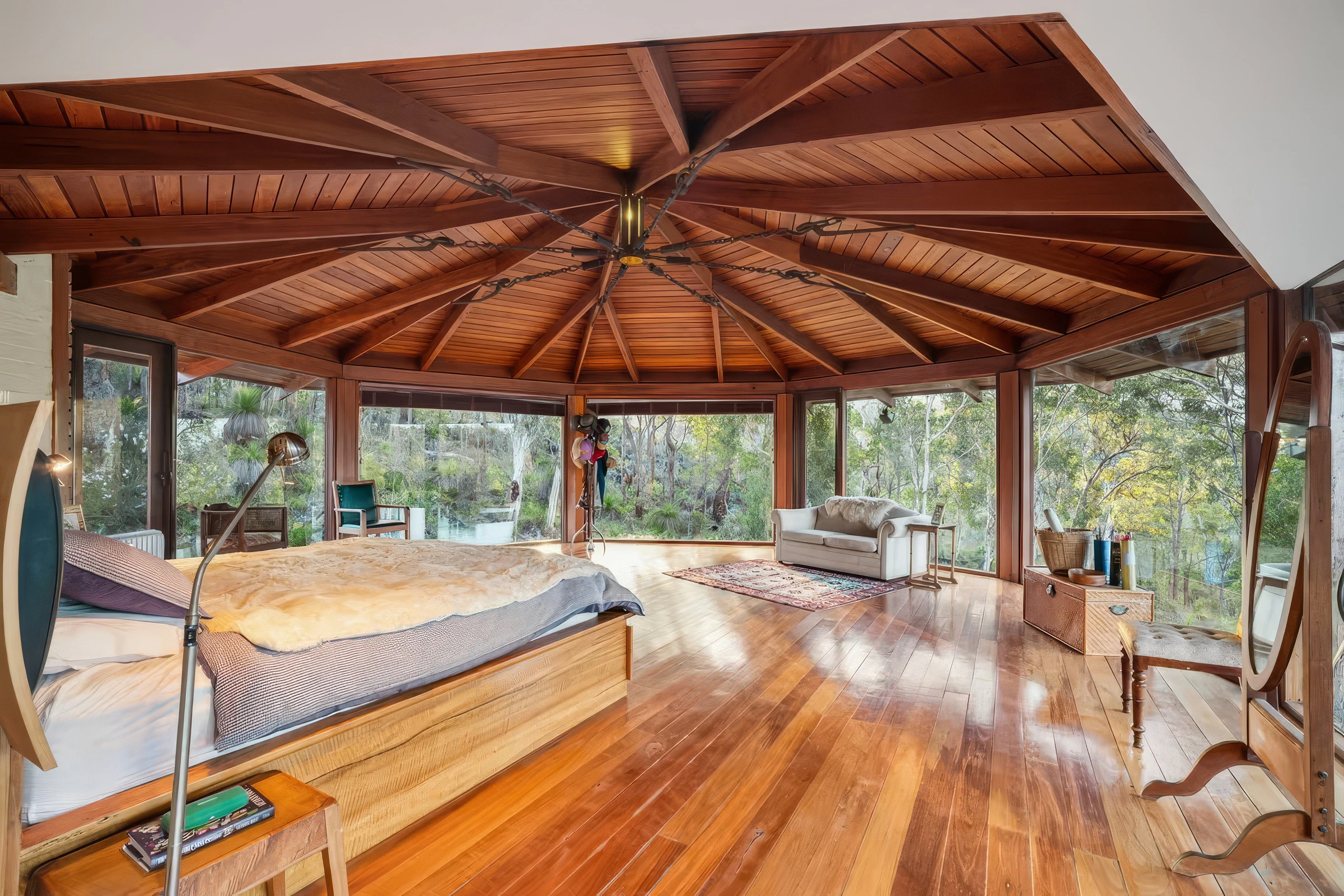 Bedroom with curved glass walls and wooden ceiling in a forest setting