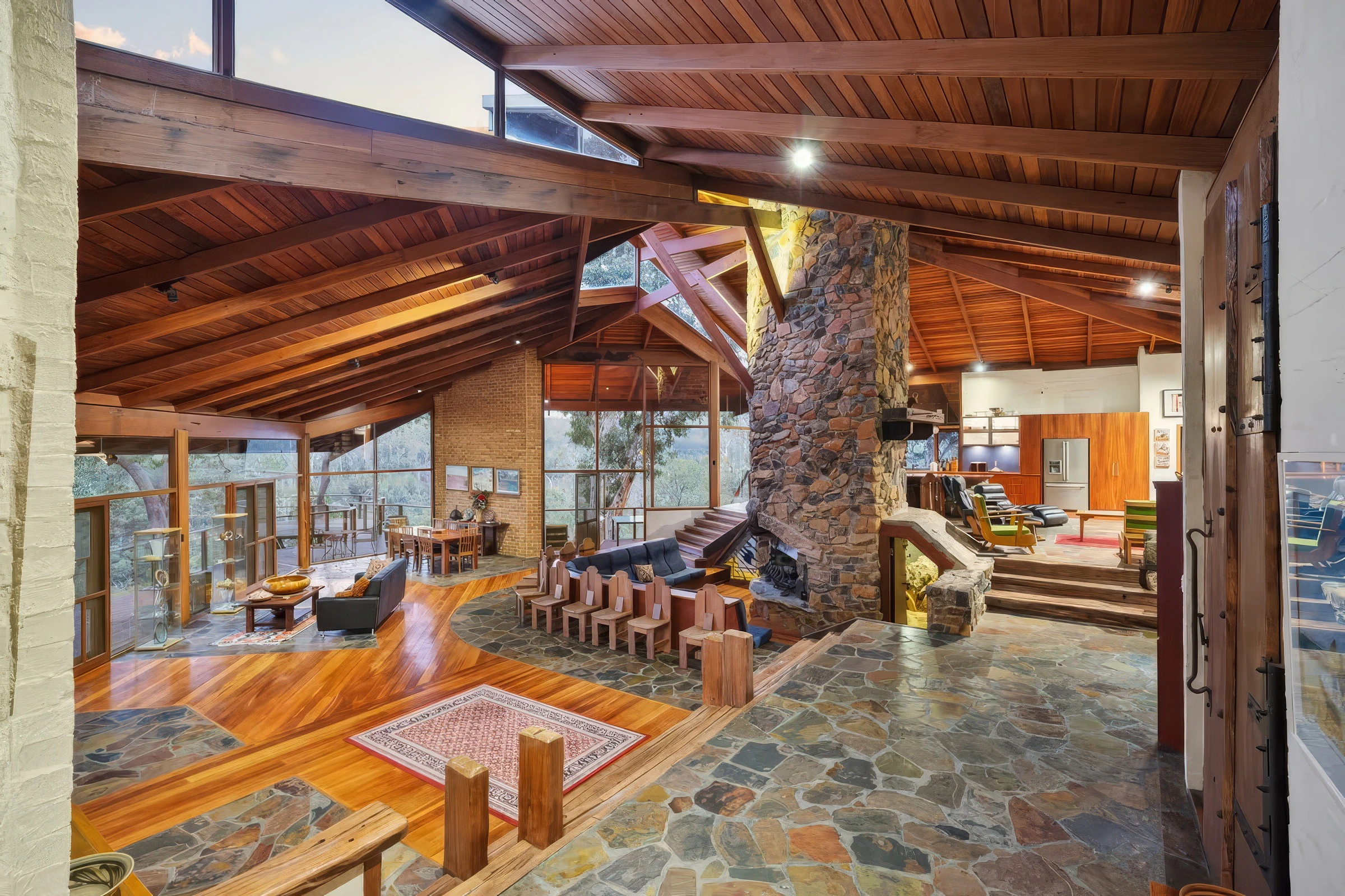 Interior of a spacious living room featuring a high wooden ceiling, stone fireplace, and floor-to-ceiling windows