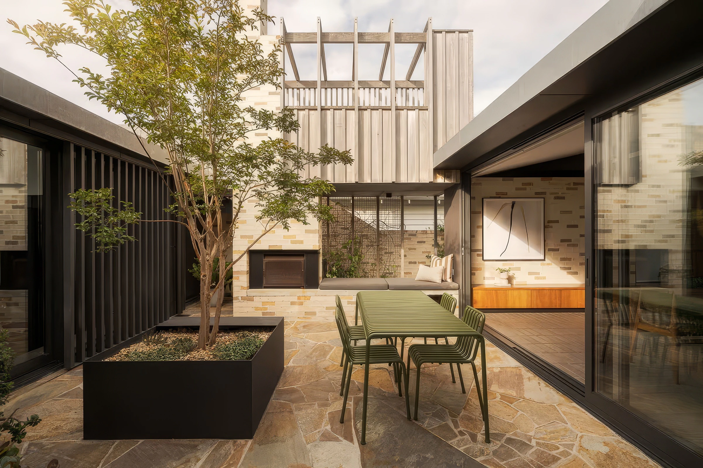 Outdoor patio area with dining table, potted tree, seating nook, and sliding glass doors leading to interior living space