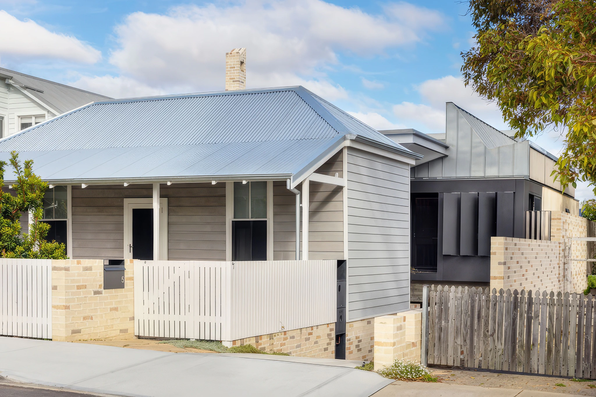 Exterior view of a modern residential house with grey siding, a metal roof, and a wooden fence
