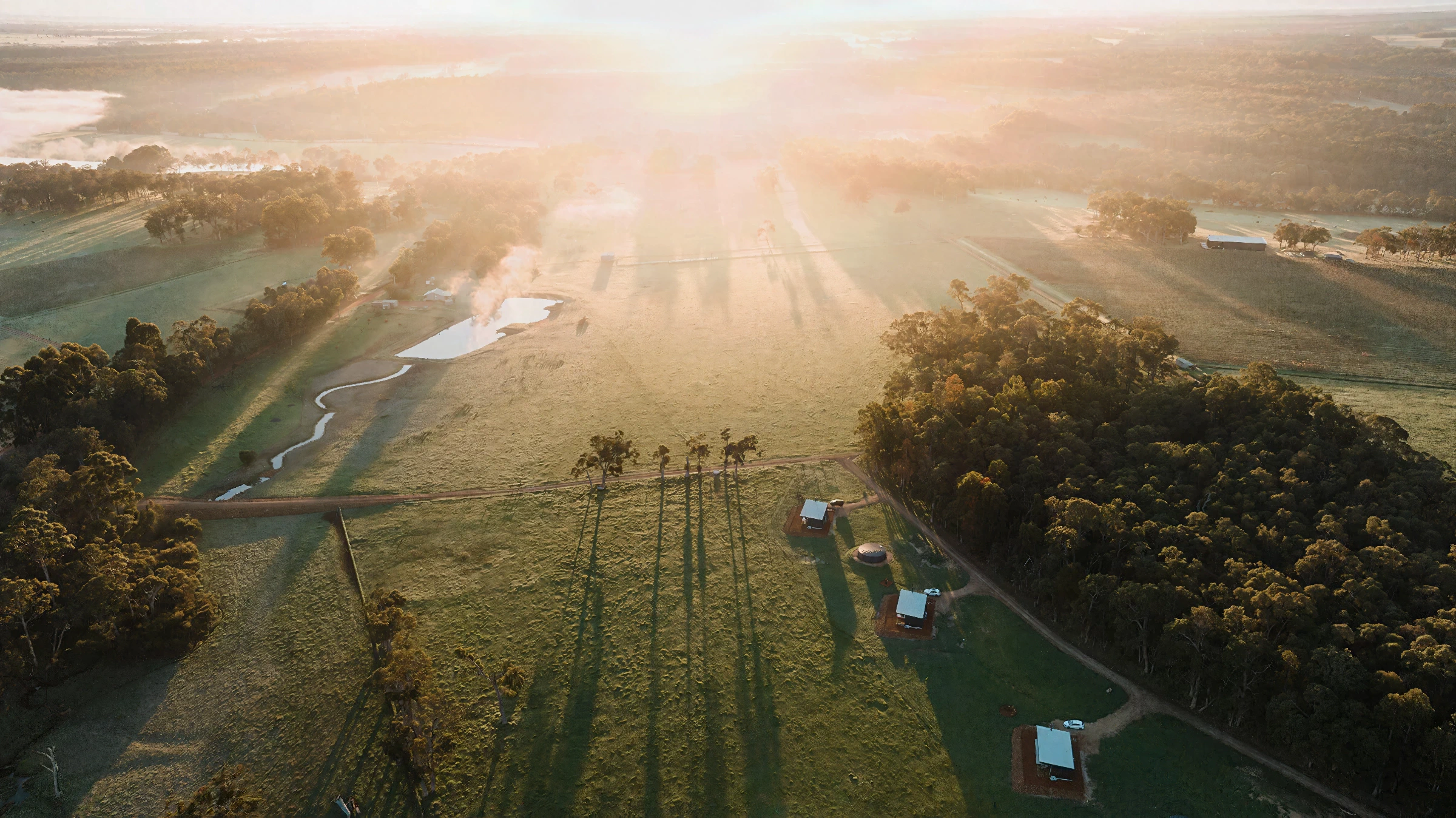 Aerial view of farmland with trees, ponds, and small buildings at sunset