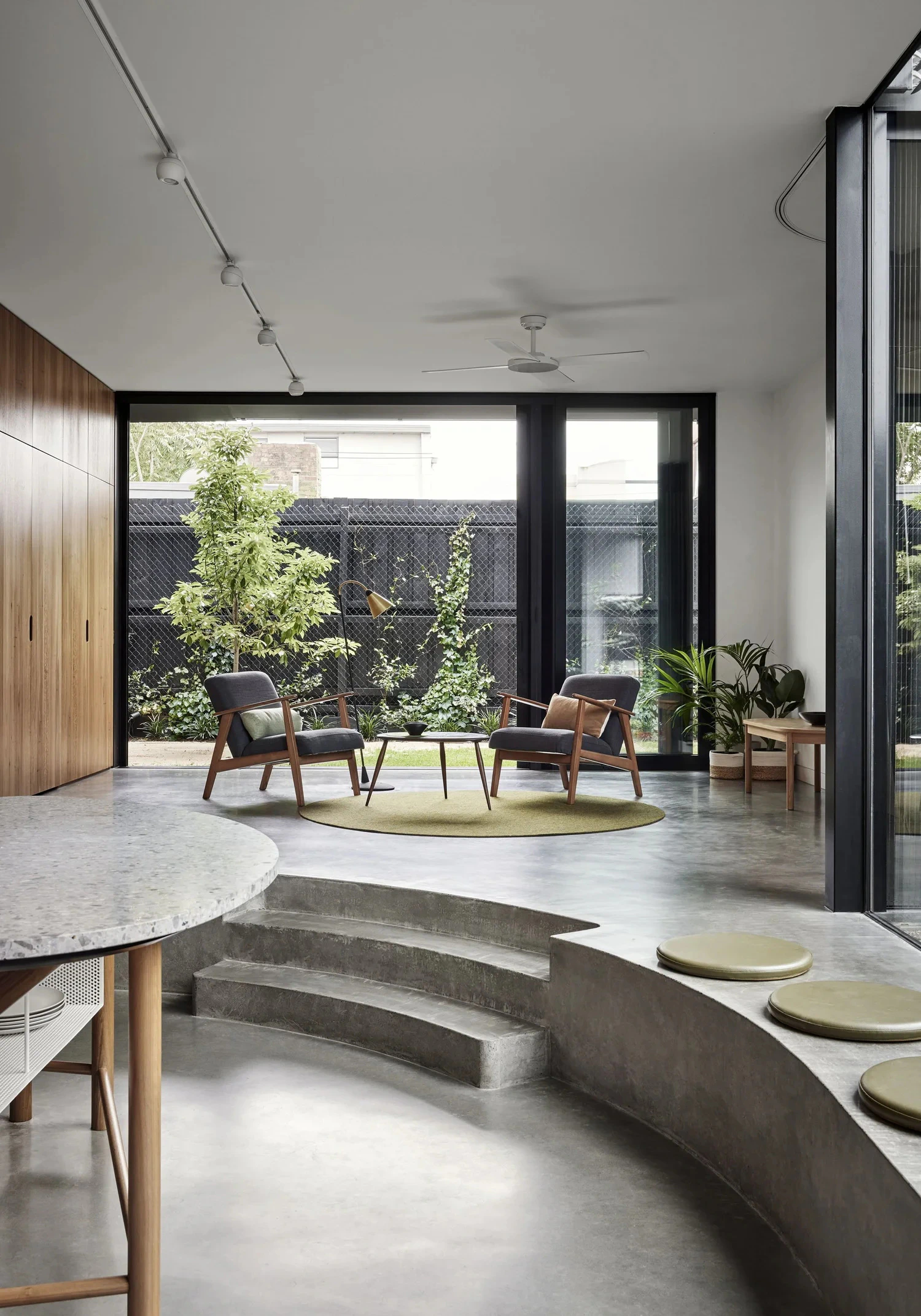 Open-plan living room featuring curved concrete steps and garden-facing glazing