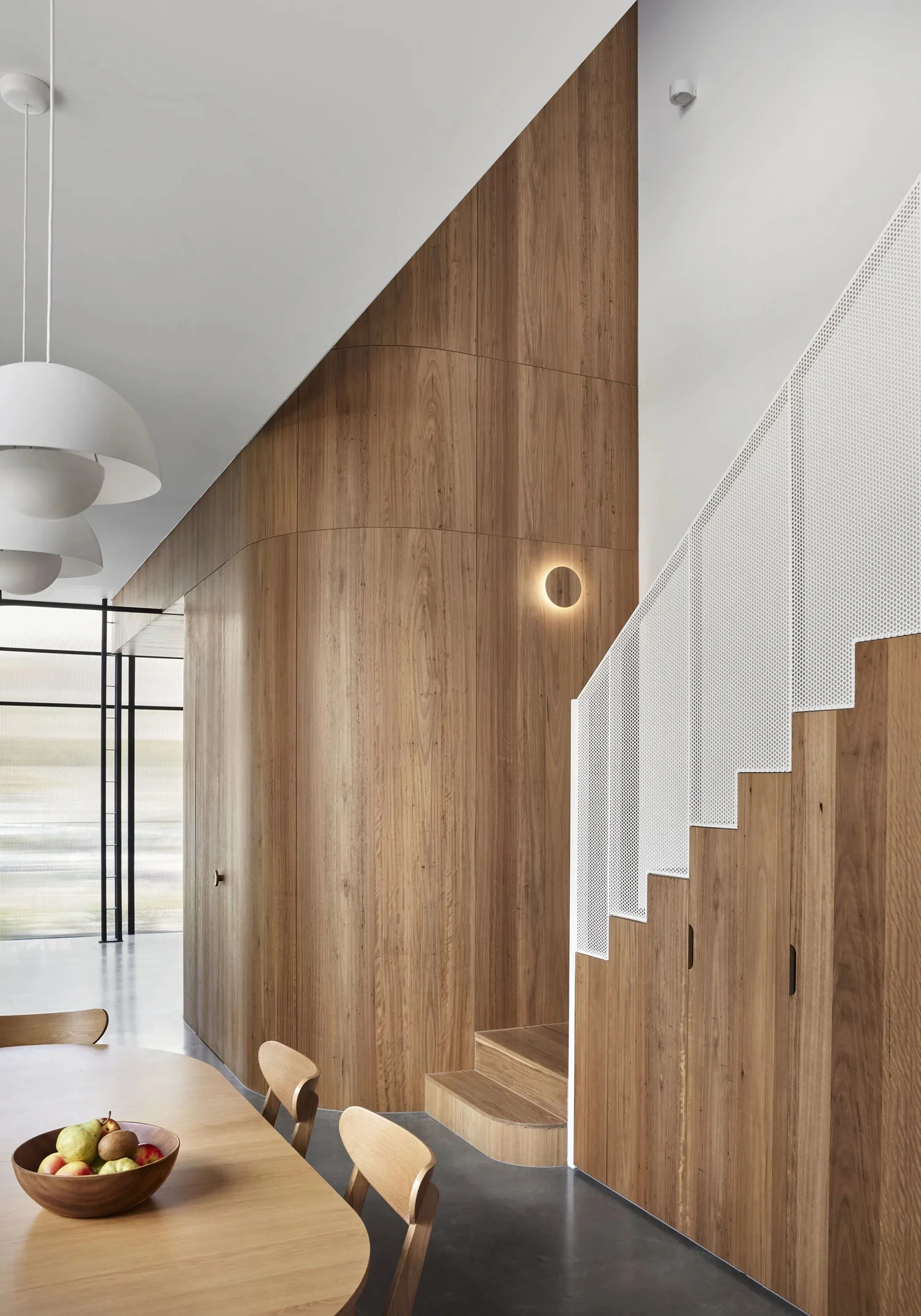 Timber staircase beside dining area and curved timber wall