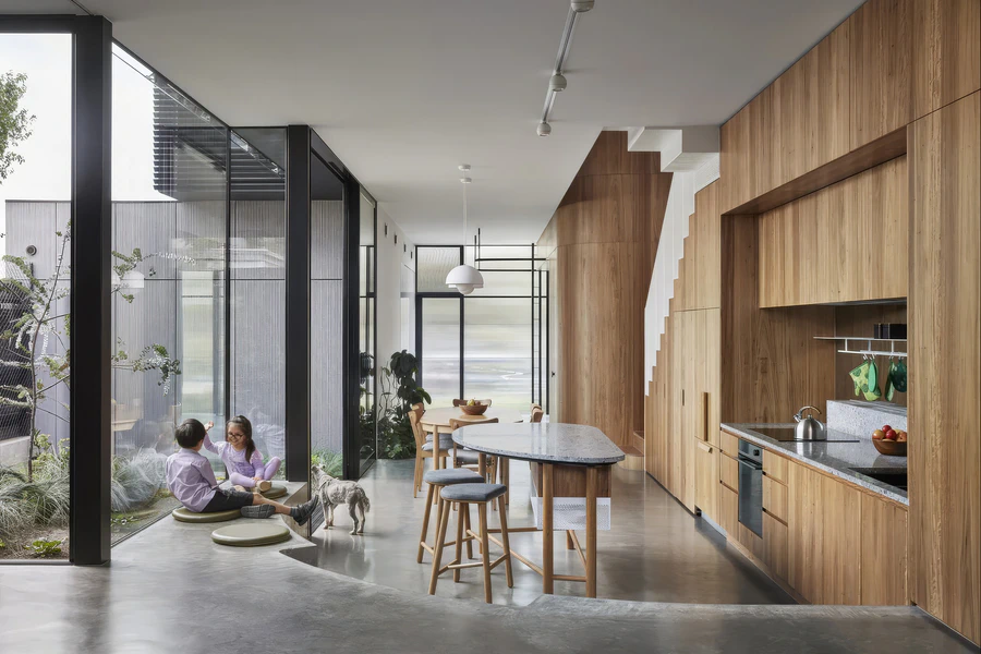 Open-plan kitchen and dining area beside floor-to-ceiling courtyard glazing