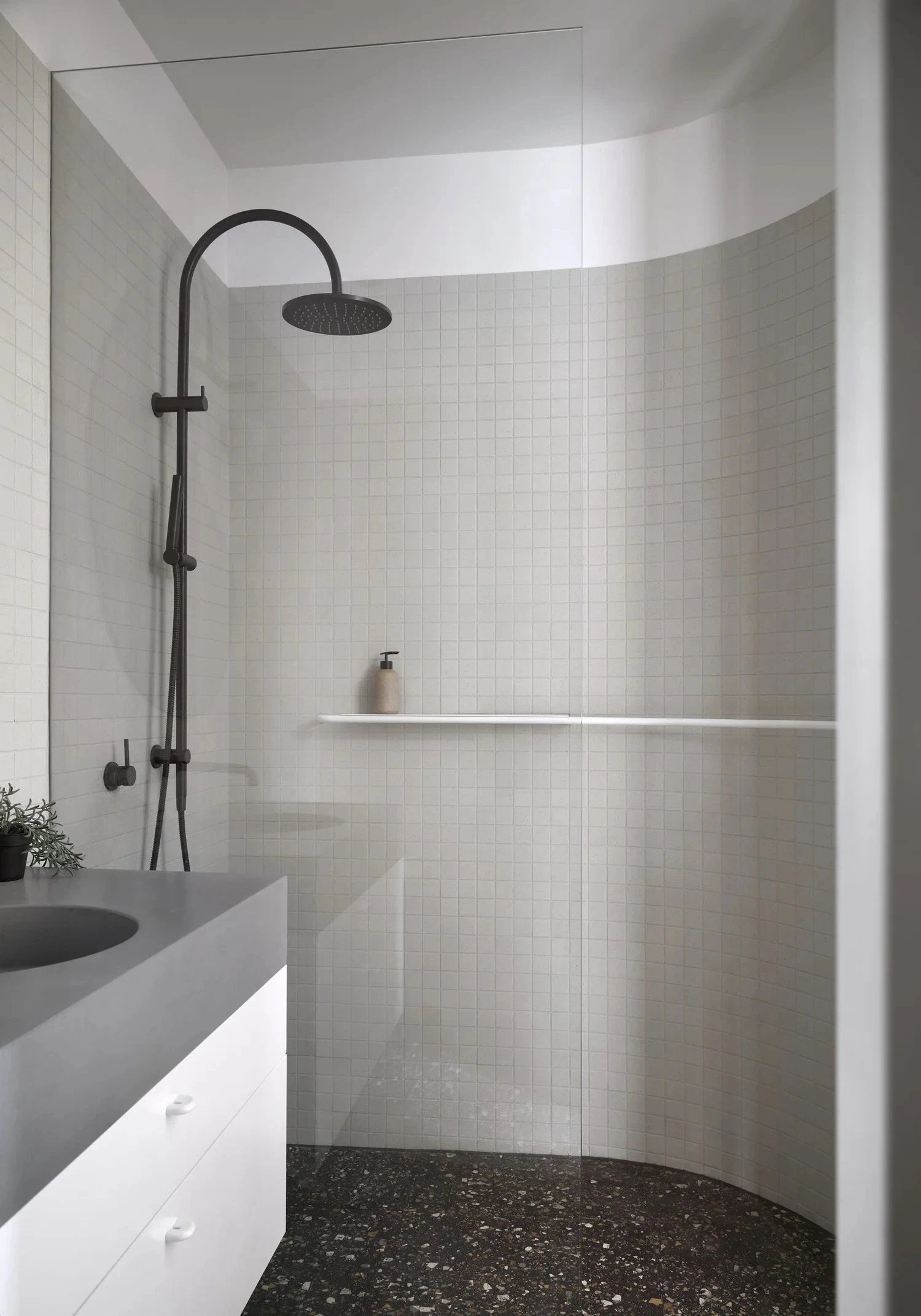 Curved tiled walk-in shower and vanity in white bathroom