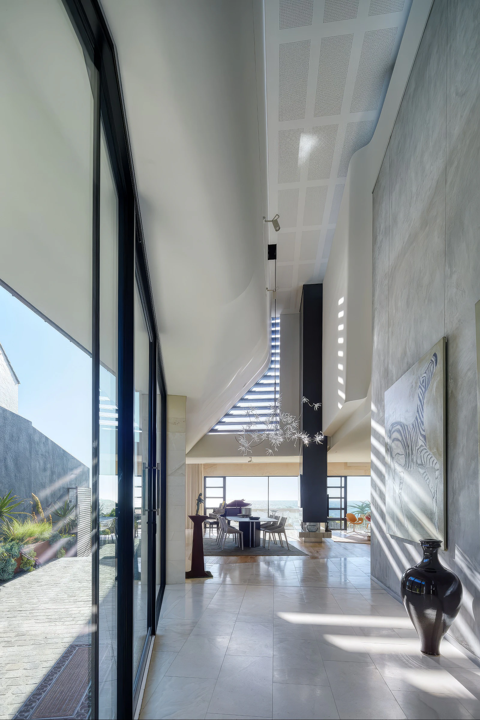 Double-height hallway and open-plan living area with skylight ceiling and large glass doors