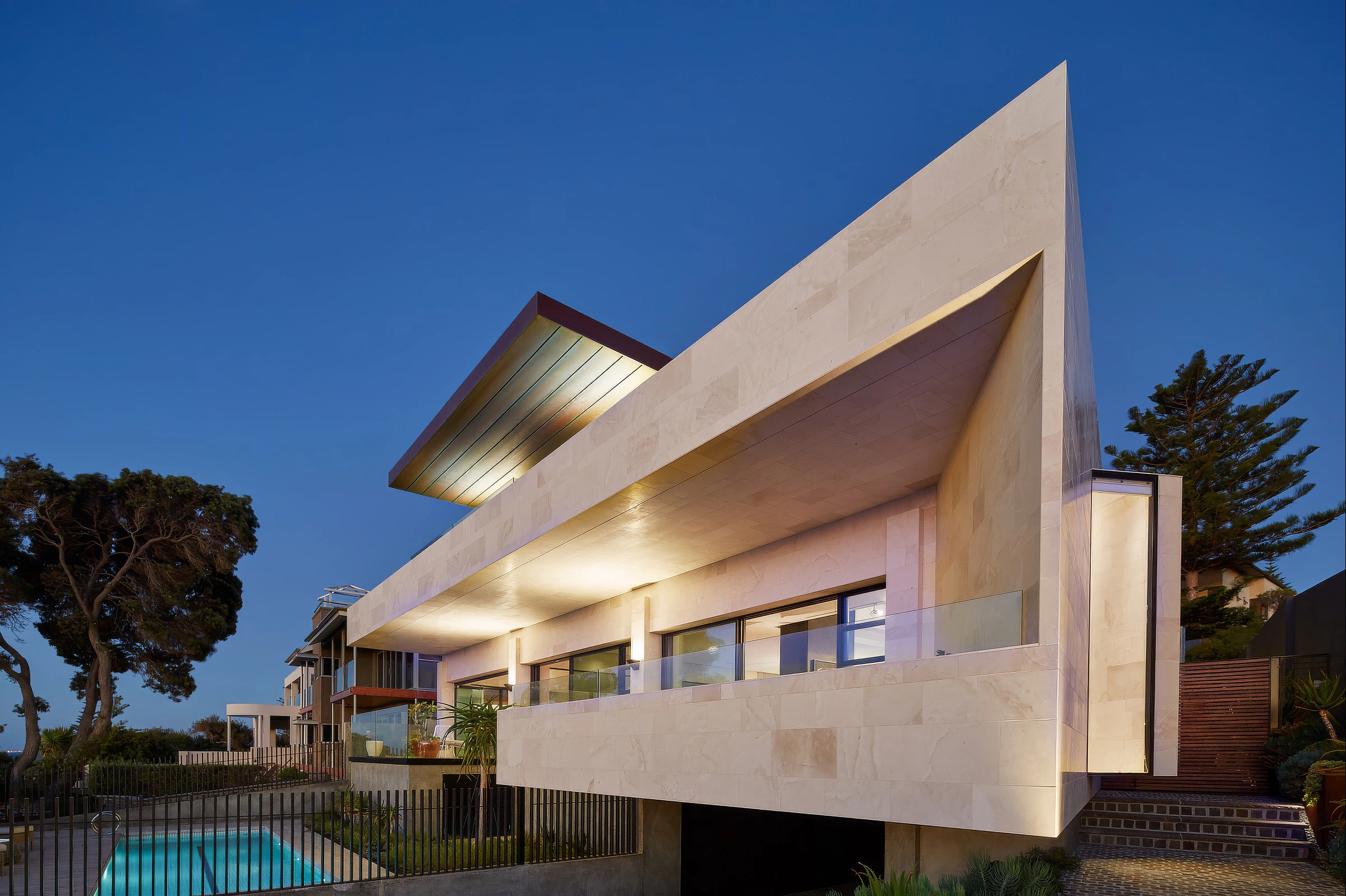 Contemporary stone house exterior at dusk above pool courtyard