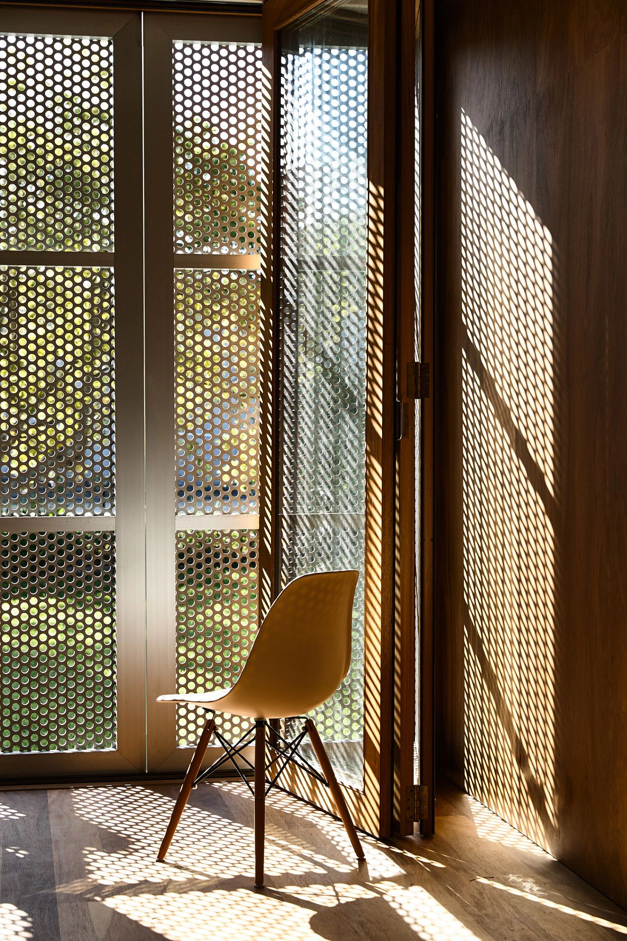 Perforated sun screens casting dotted shadows across timber beach house interior