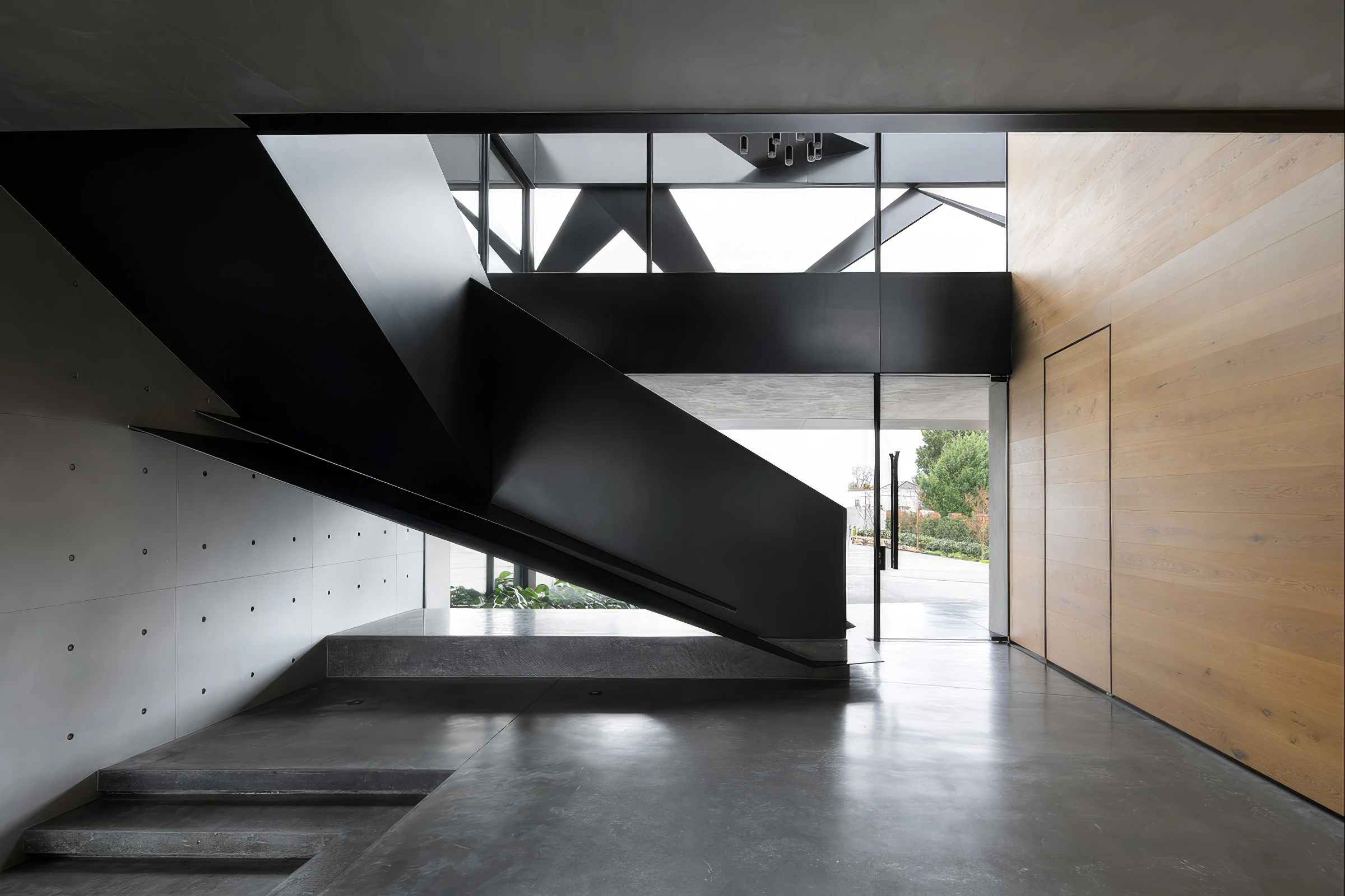 A folded black stair slices diagonally through pale concrete surfaces