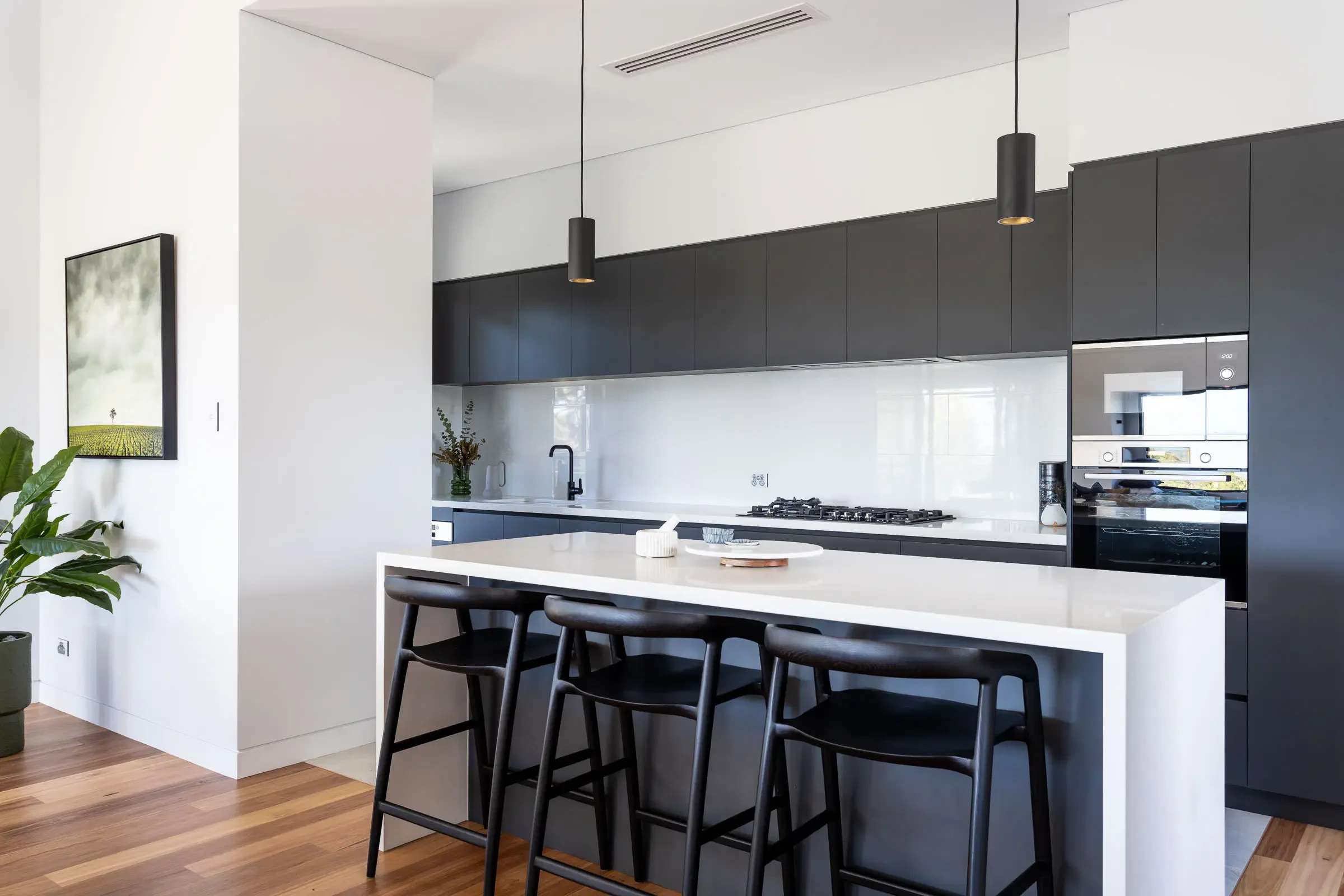 Minimalist black and white kitchen with island, black bar stools, built-in appliances, and modern lighting