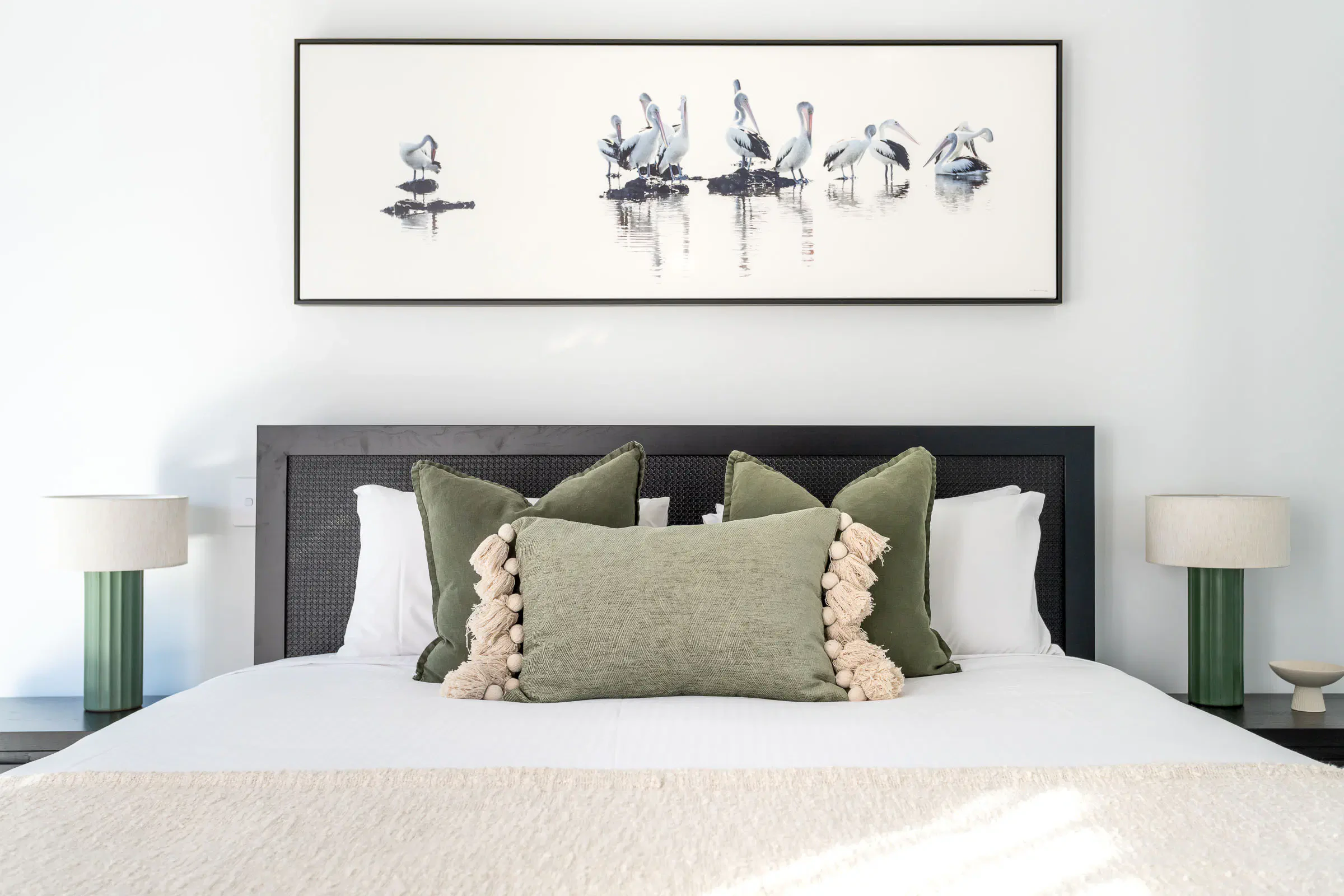 Bedroom with framed bird artwork above bed featuring green and beige cushions