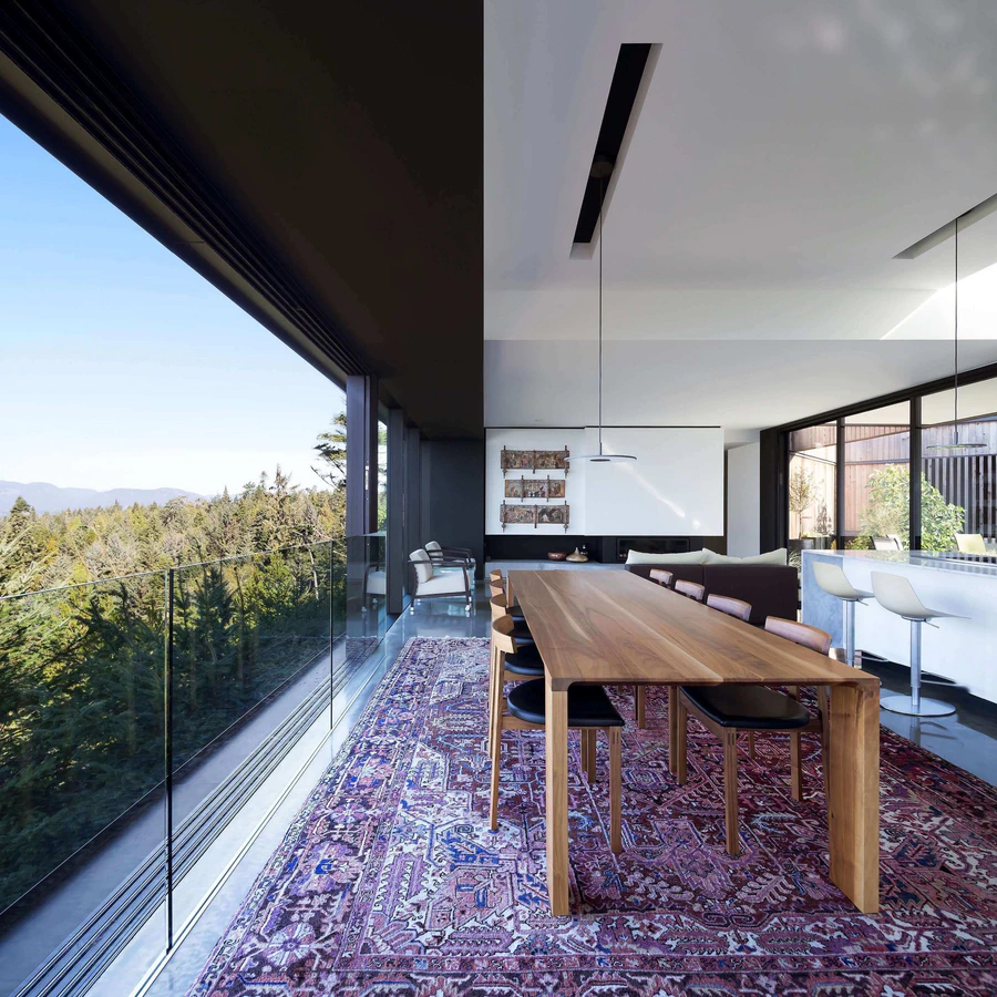 Open-plan dining and living area with large glass windows overlooking a forested landscape
