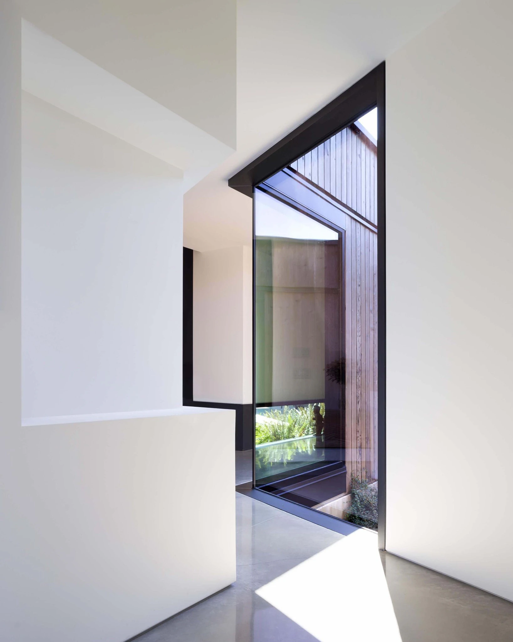 Interior view of a modern minimalist entryway with a large glass door and wooden exterior siding