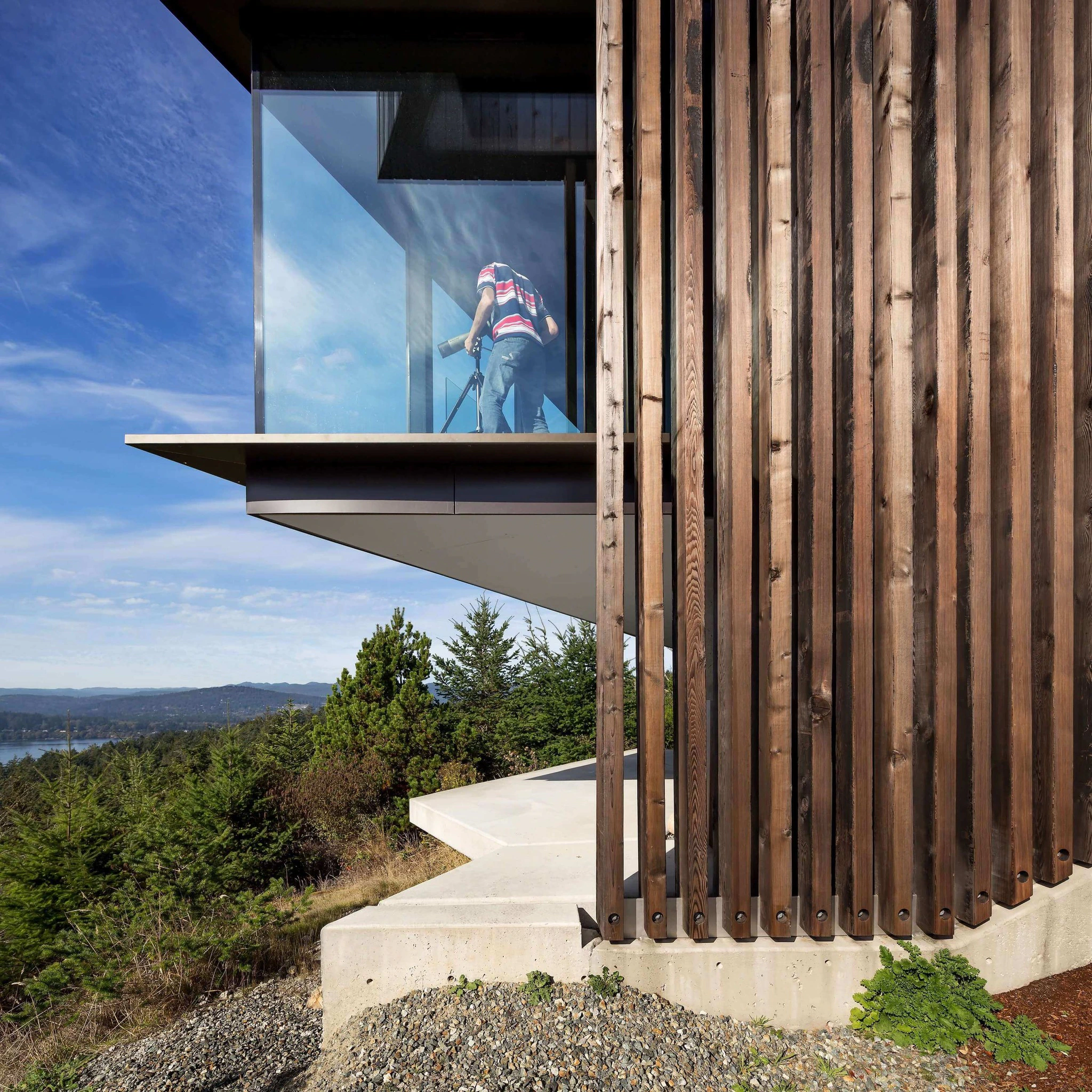 Modern residential building with wooden exterior cladding and large glass window overlooking natural landscape