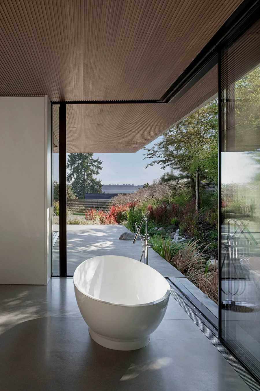 Freestanding bathtub beside floor-to-ceiling window overlooking garden courtyard