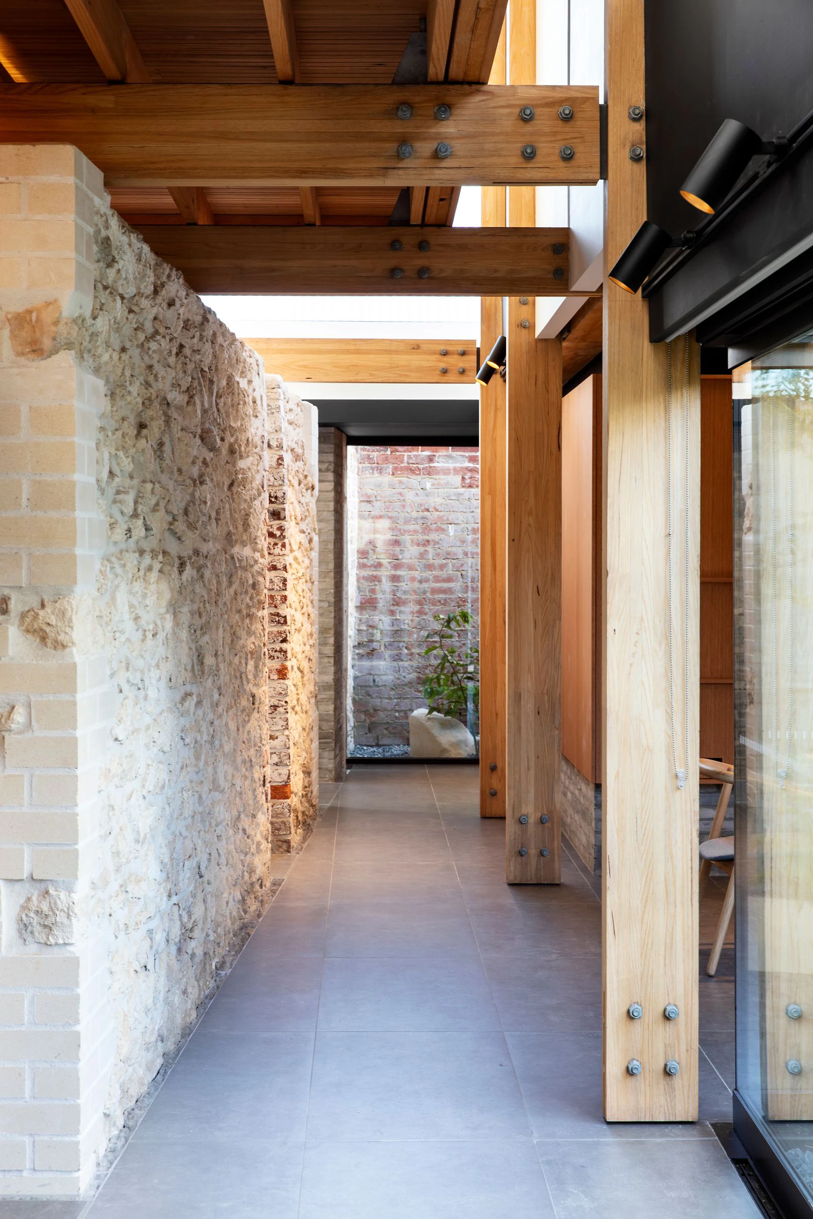 Interior corridor with exposed brick and stone wall, wooden beams, and modern sliding glass door interaction.