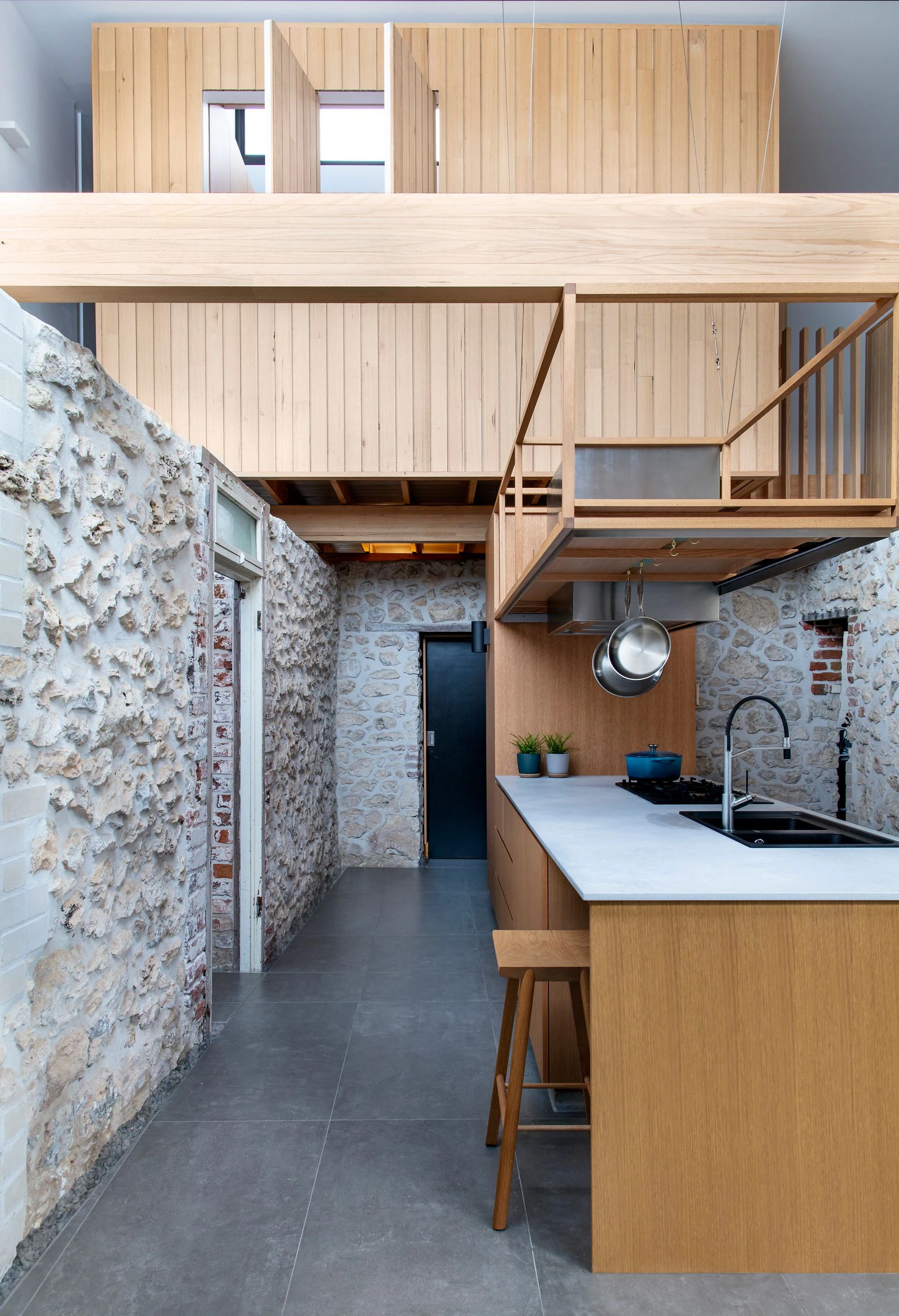 Open-plan kitchen with stone and brick walls, wooden cabinetry, and a loft space.