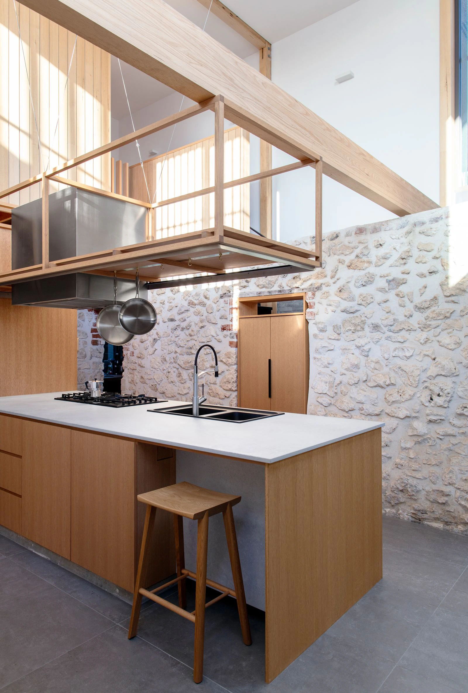 Wooden kitchen island with sink and stove, stone wall backdrop, and hanging pots in a modern rustic style kitchen