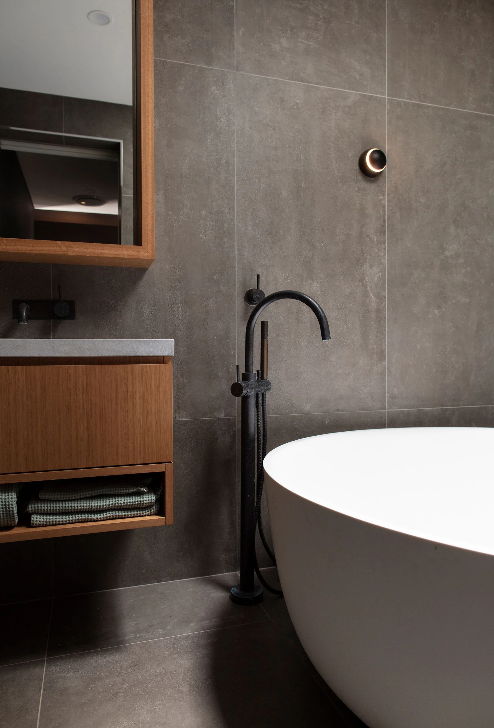 Modern bathroom with dark tiled walls, a freestanding bathtub, and wooden cabinetry