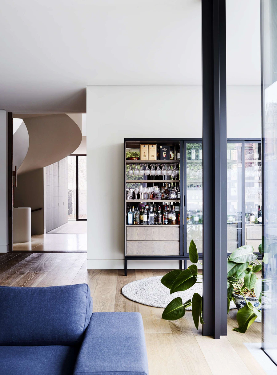 Modern interior living space with a bar cabinet, large window, green indoor plant, and blue sofa