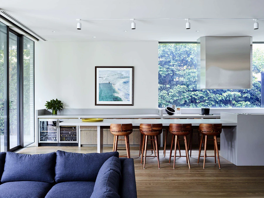 Contemporary kitchen and living area with bar stools and large window overlooking greenery