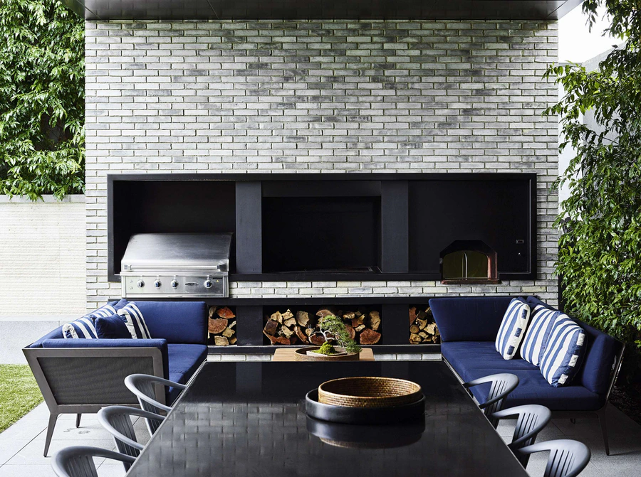 Outdoor living area with brick wall, built-in BBQ, and seating with navy cushions