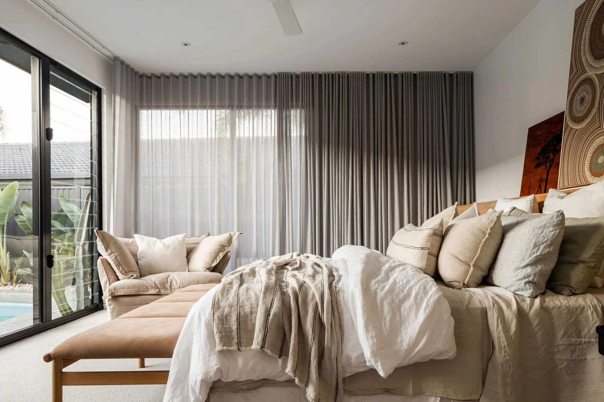 Bedroom interior with large windows, sheer curtains, and bed with cushions