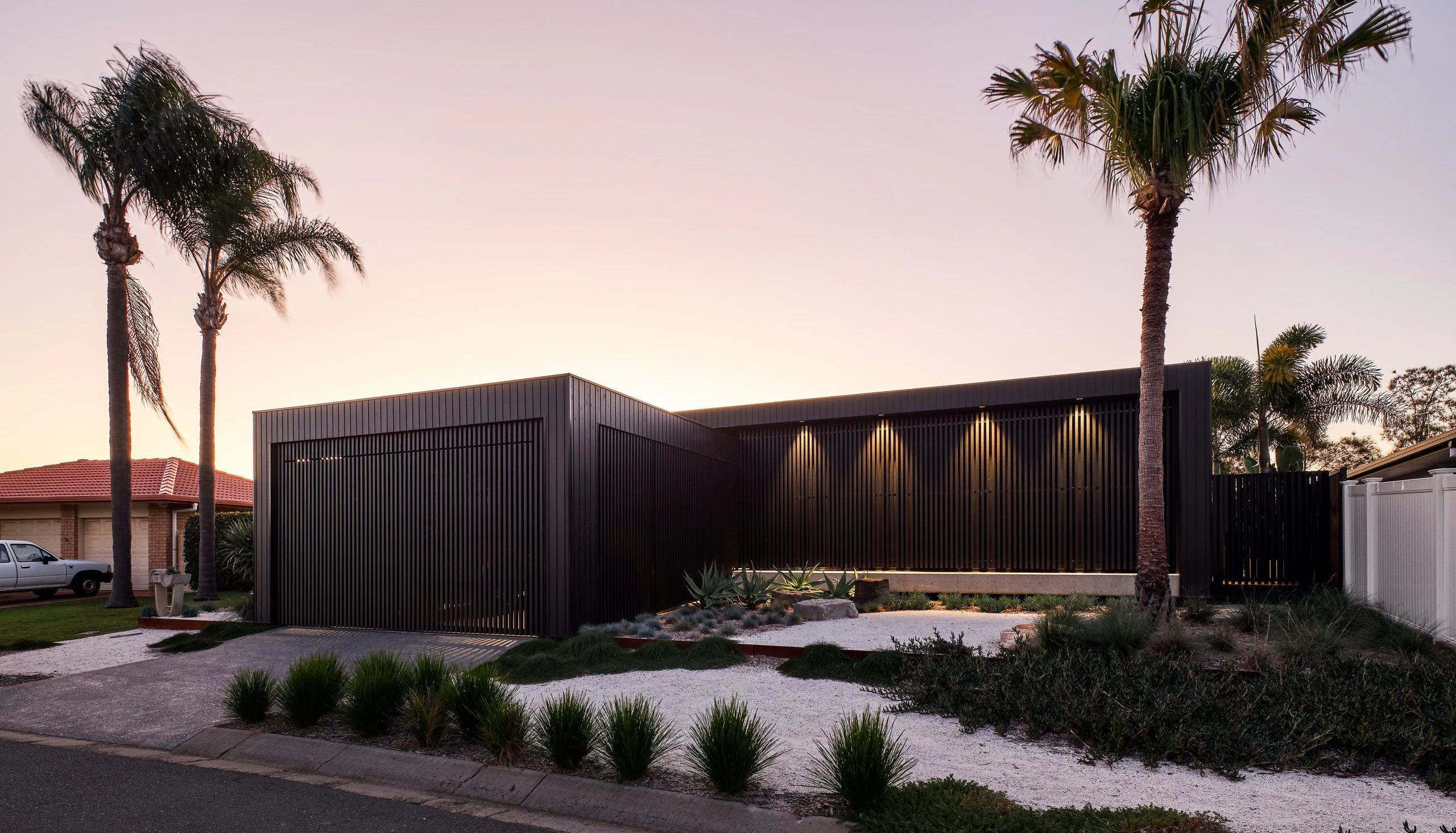 The front garden is deliberately spare against the blackened shell of The Kira House