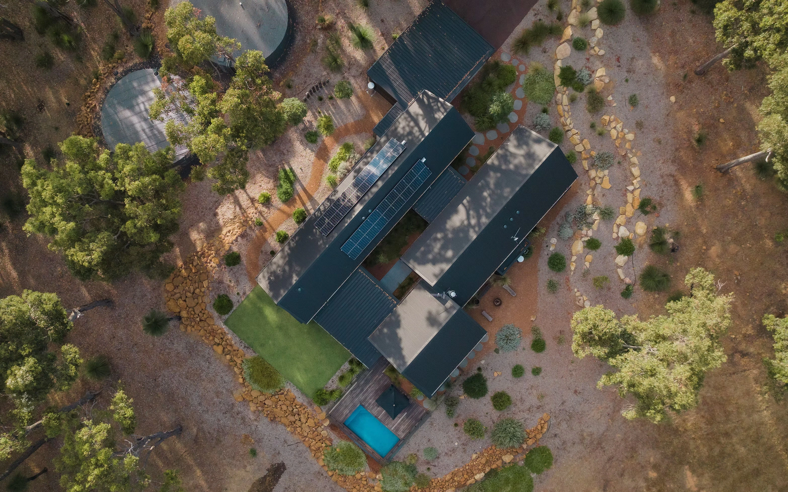 Aerial view of a modern house with solar panels, swimming pool, and landscaped yard surrounded by trees