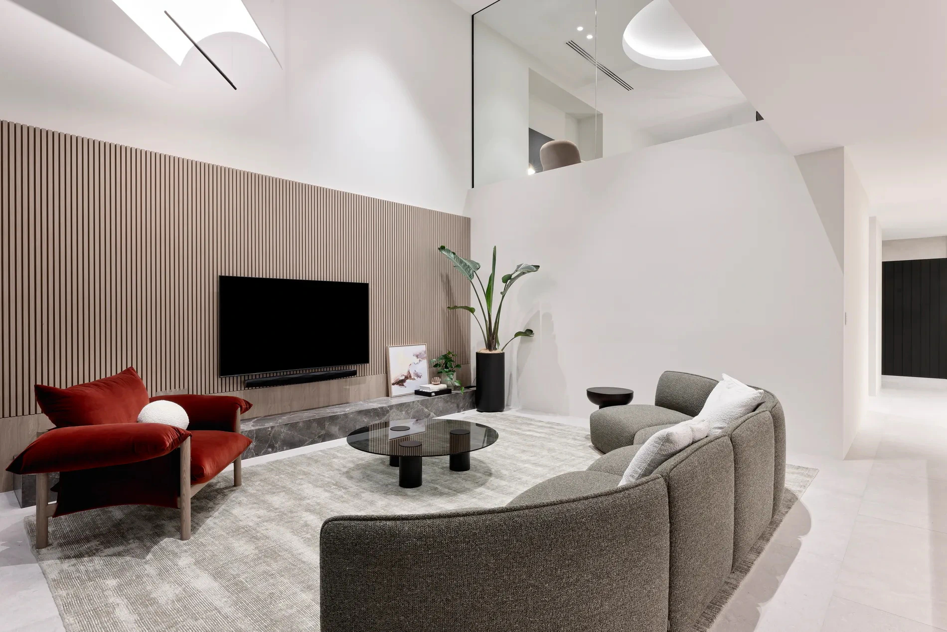 Modern living room with curved sofa, red armchair, and wall-mounted flat-screen TV