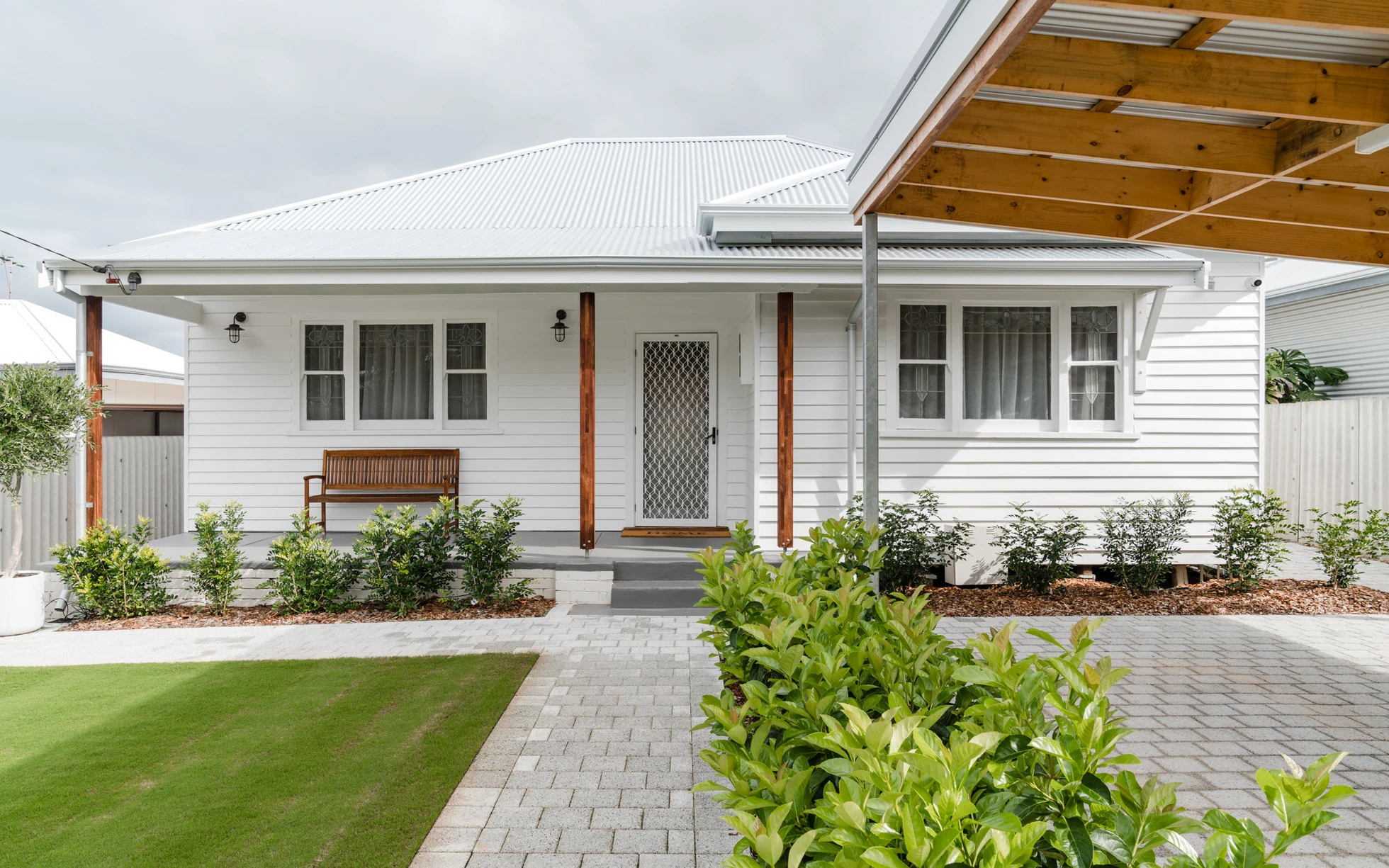 Single-storey house with white exterior and metal roof in suburban backyard