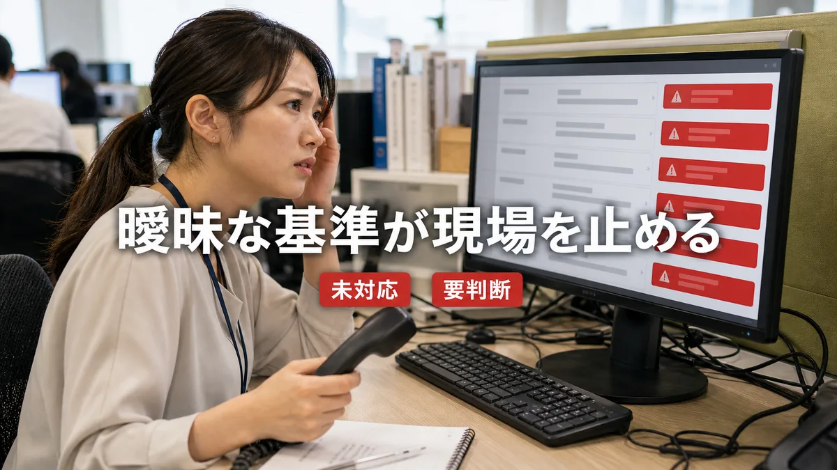 オフィスのデスクでPC画面の問い合わせ一覧を前に困惑した表情を浮かべる現場の担当者