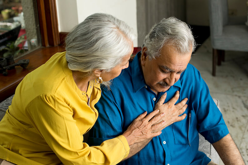 Older adult man having a heart attack while wife comforts him. 