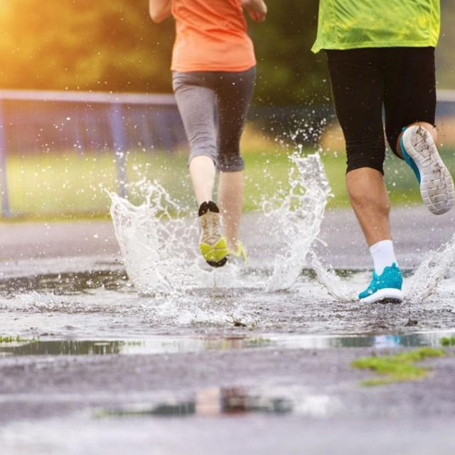 Two runners splashing through puddles on a wet road, seen from behind