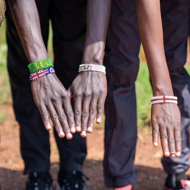 Three young Kenyan runners holding out their hands, each wearing a beaded band