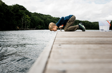 Young Girl Standing In Water At Lake Holding Fishing Pole by Cavan Images