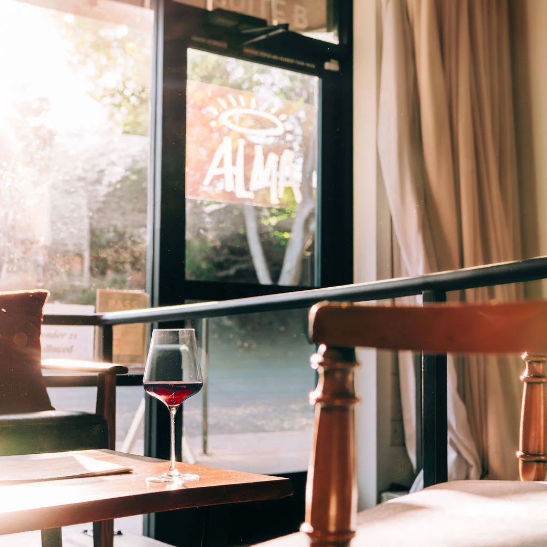 Photo of interior of Alma where you can see the logo on the front door. It is sunset and there is a glass of wine resting on a table