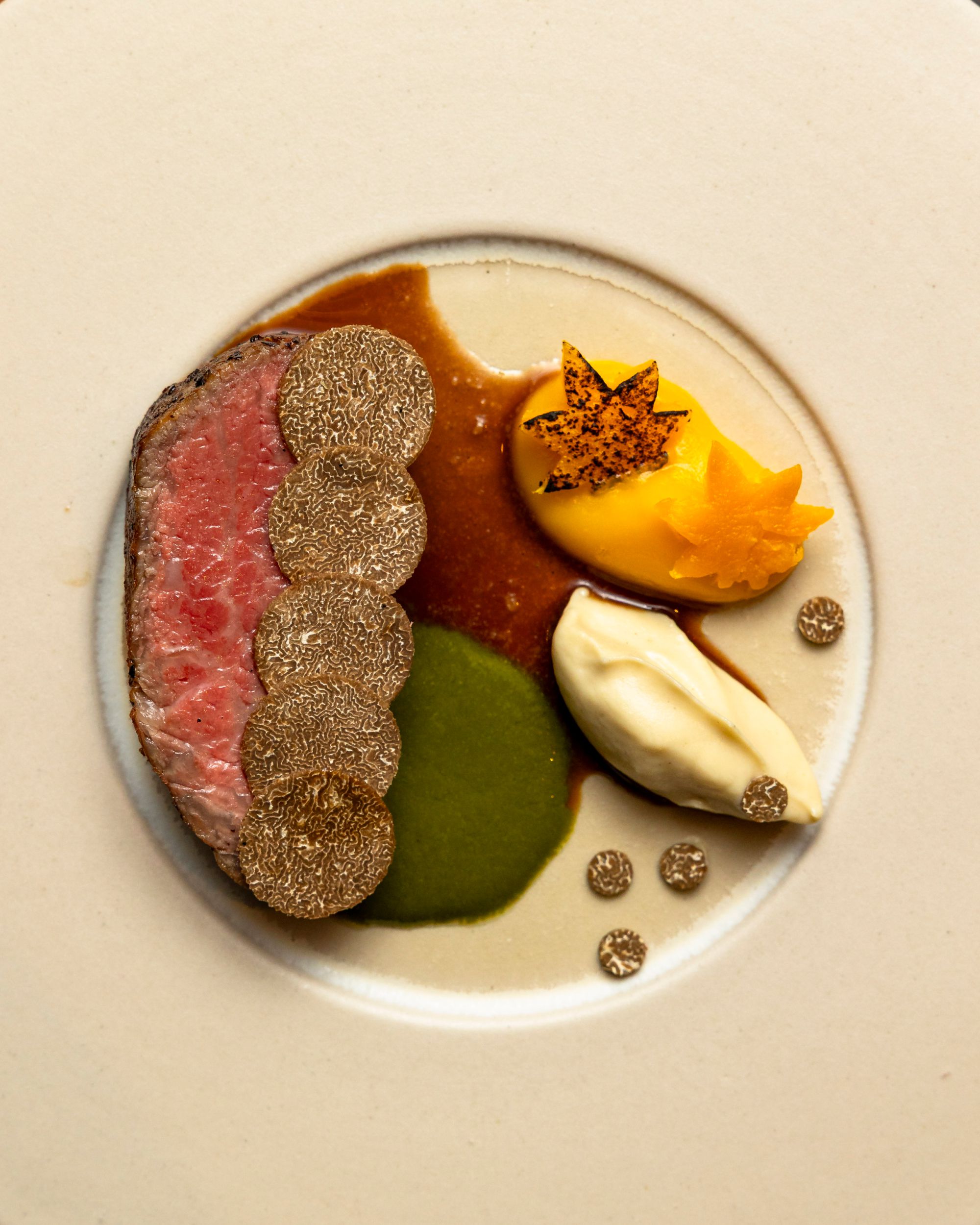 A dish consisting of wagyu and truffles plated with various sauces
