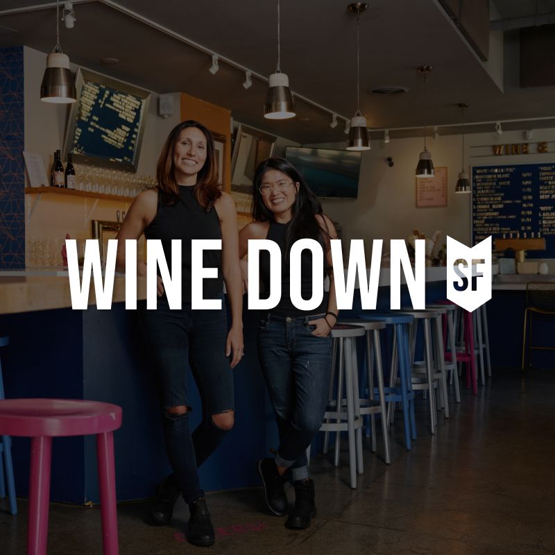 Logo of Wine Down SF on background of the owners standing in the Wine Down space.