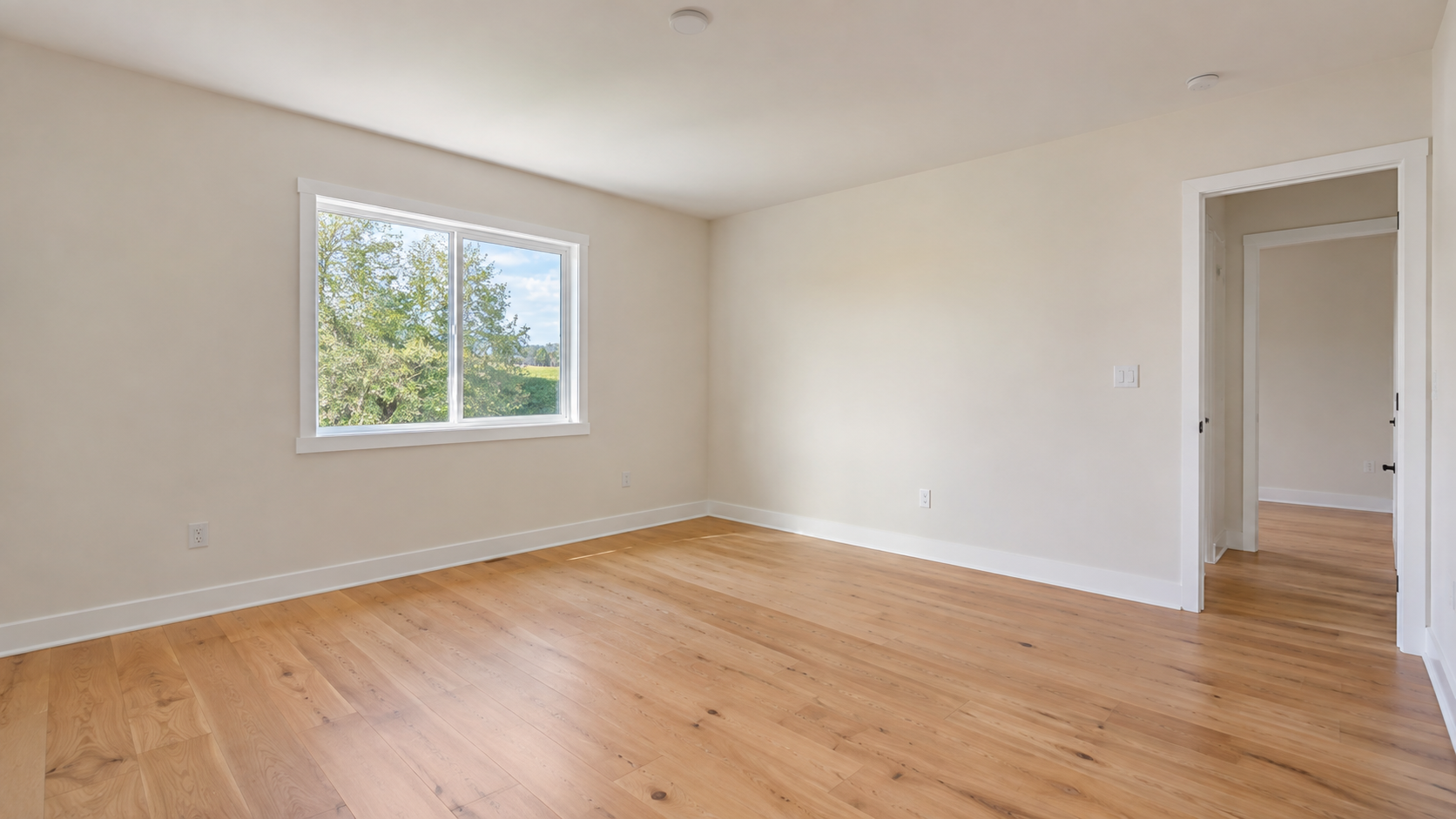 Empty primary bedroom before virtual staging with wood flooring, a window, and an open doorway