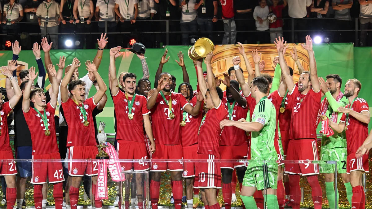Jamal Musiala of FC Bayern Munich celebrates with a wide smile, holding the DFB Pokal trophy.