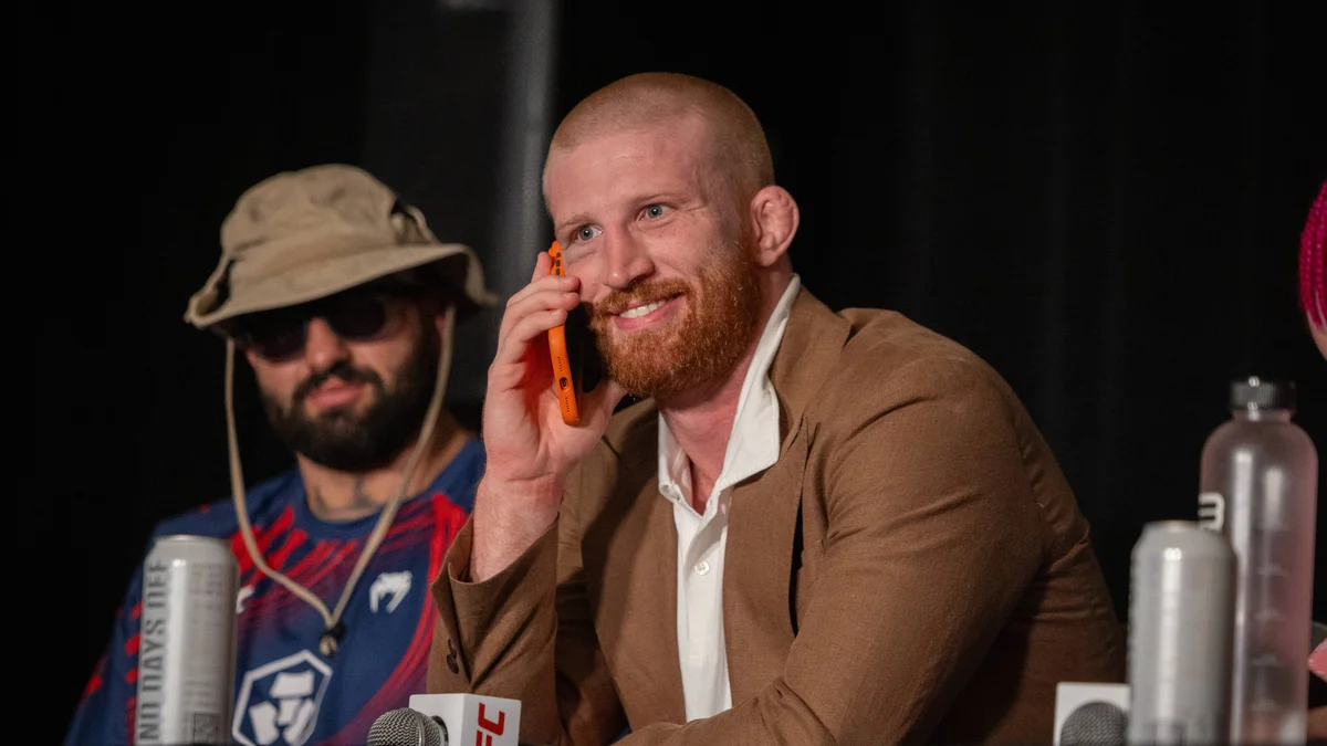 Bo Nickal speaks on the phone at a UFC press conference, with Dana White and other fighters nearby.