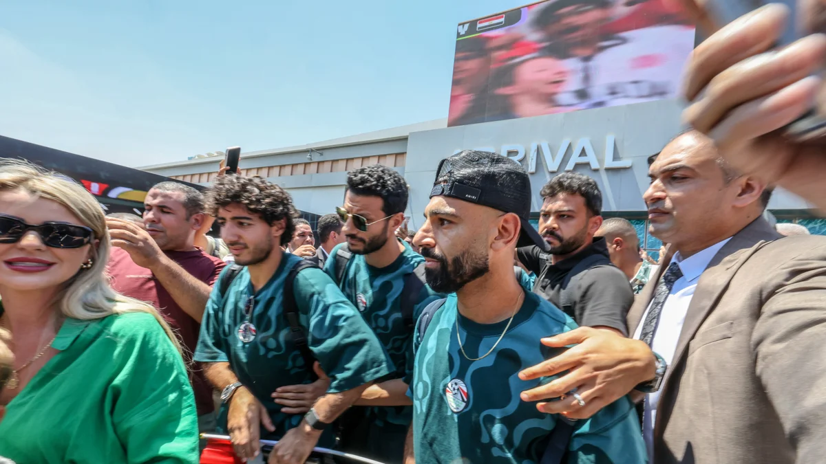 Mohammed Salah, wearing a suit, is greeted by cheering fans at El-Alamein Airport after Egypt's World Cup elimination.