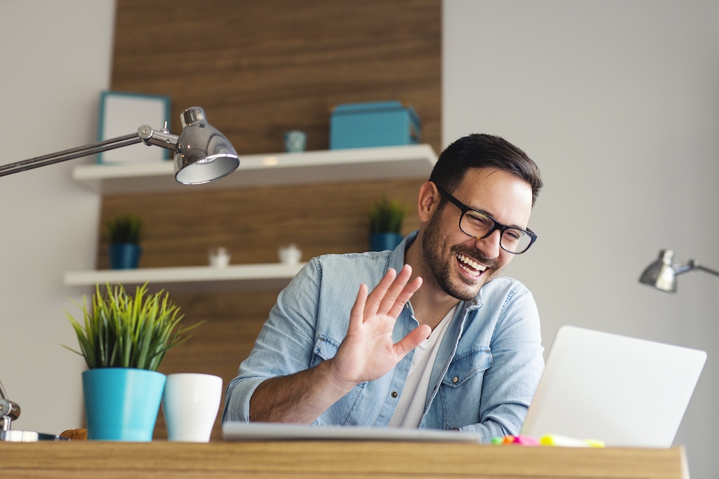 Man waving at laptop on video call software