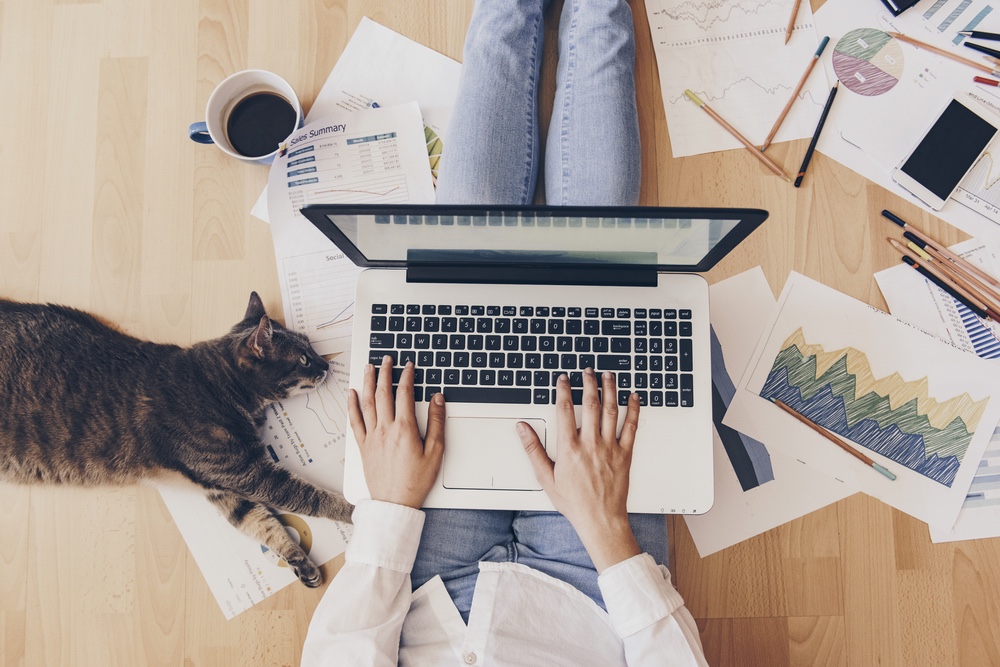 Woman typing on floor with cat collaborating with her team from home