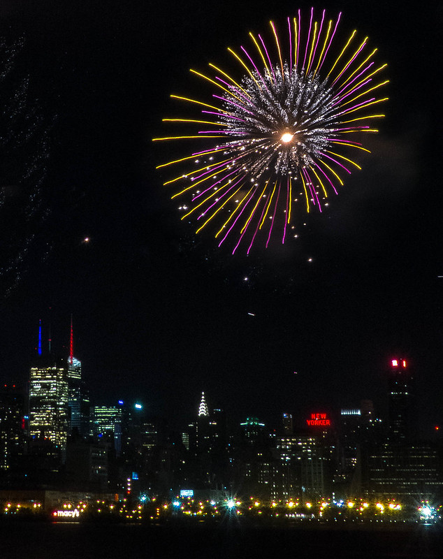 Fireworks Photography 101: long exposure of a single symmetrical gold and magenta firework burst over an illuminated city skyline at night