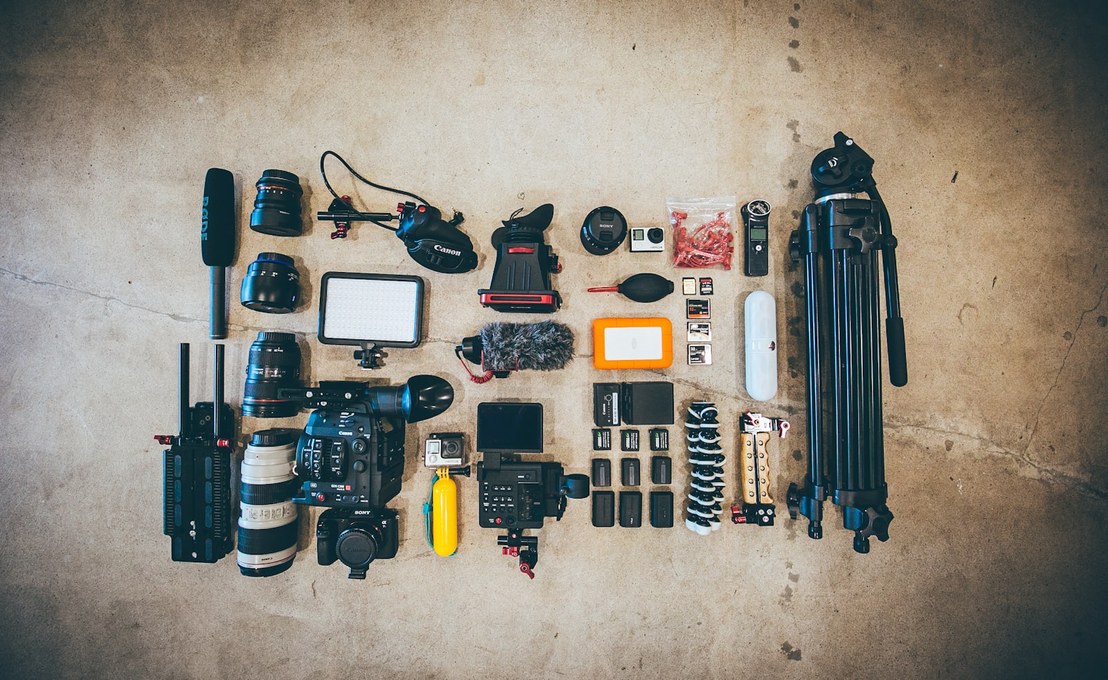 flat lay of camera body, lenses, tripod, microphone and various accessories arranged on a floor