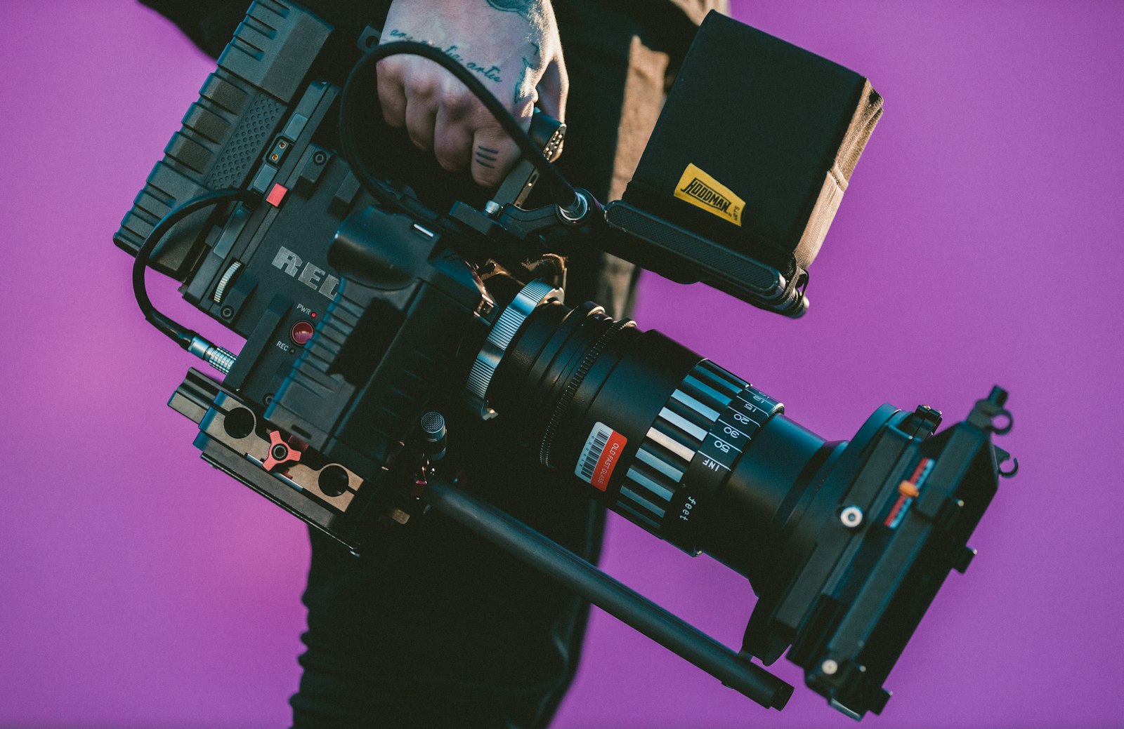 person holding a professional cinema camera with lens against a purple background
